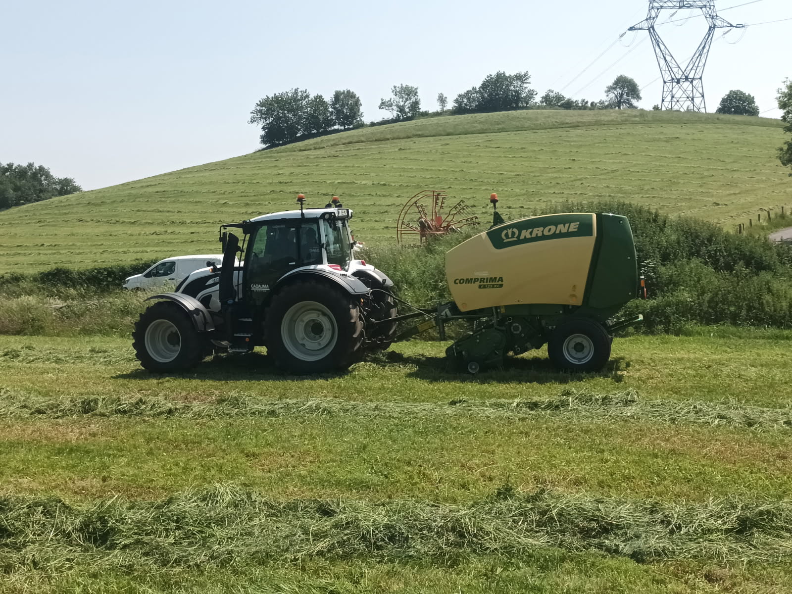 Tracteur avec presse Krone au travail dans un champ de foin, md-services-mecanique-hydraulique-aveyron en Aveyron